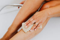 Femme exfoliant sa jambe sous la douche avec un gant exfoliant pour une peau lisse
